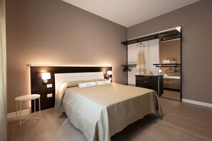 Quarto de hotel moderno com uma cama grande, mesas de cabeceira, guarda-roupa e um espelho.