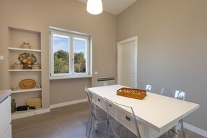 Cocina moderna con encimera blanca, sillas traslúcidas y ventana con vista a árboles.