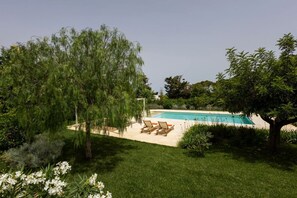 Piscina con sillas de descanso, rodeada de exuberante follaje y árboles.