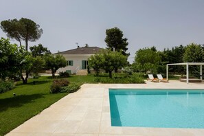 Una piscina con agua cristalina azul, rodeada por un césped cuidado y árboles.