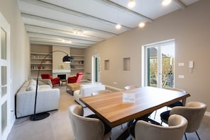 Ein modernes Wohnzimmer mit einem Holzesstisch, beigen Sofas, einem roten Sessel und einem Bücherregal.
