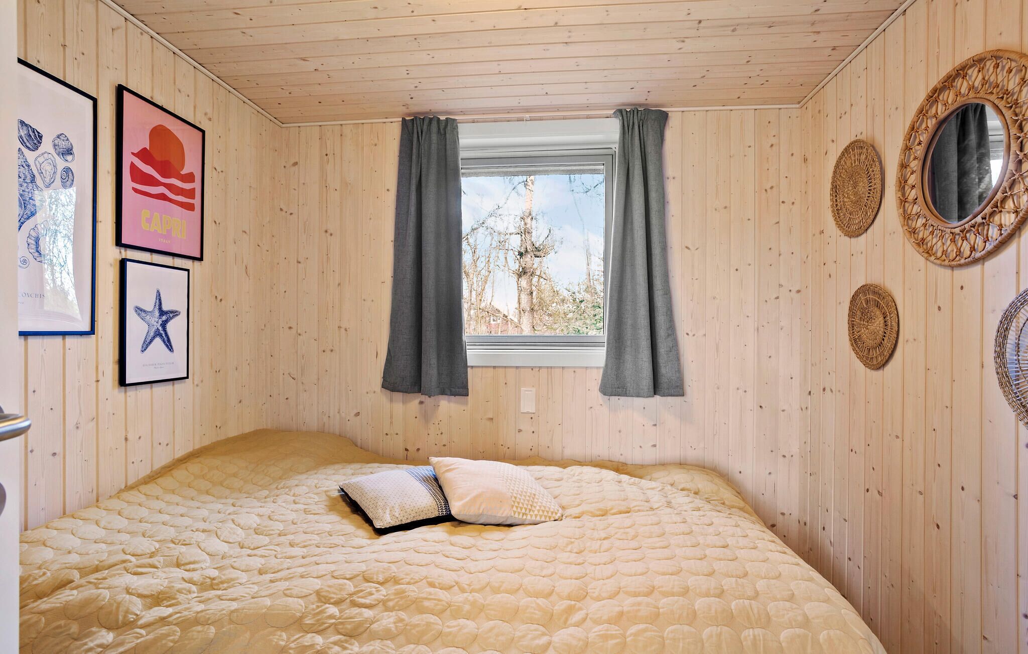 Un dormitorio con cama, ventana con cortinas, paredes de madera y cuadros enmarcados.