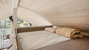 Une chambre avec un plafond en pente, un lit recouvert d’une couverture à motifs floraux et une vue sur l’extérieur par une fenêtre.