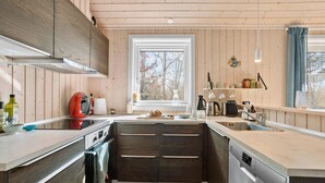 Une cuisine moderne avec des meubles en bois, un four encastré, un lave-vaisselle et une fenêtre donnant sur la forêt.