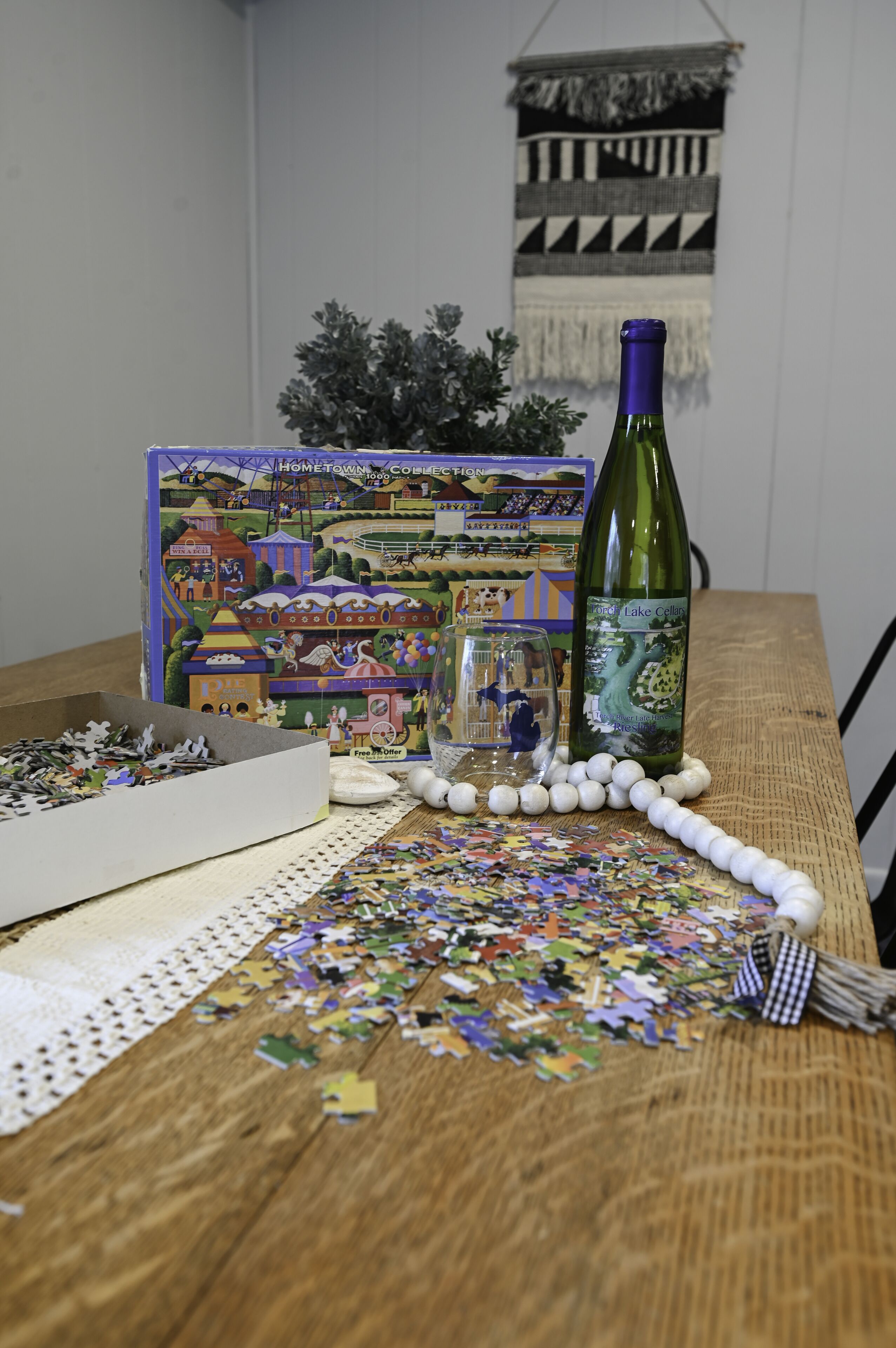 Una mesa de madera con un rompecabezas, una botella de vino y una copa pequeña.
