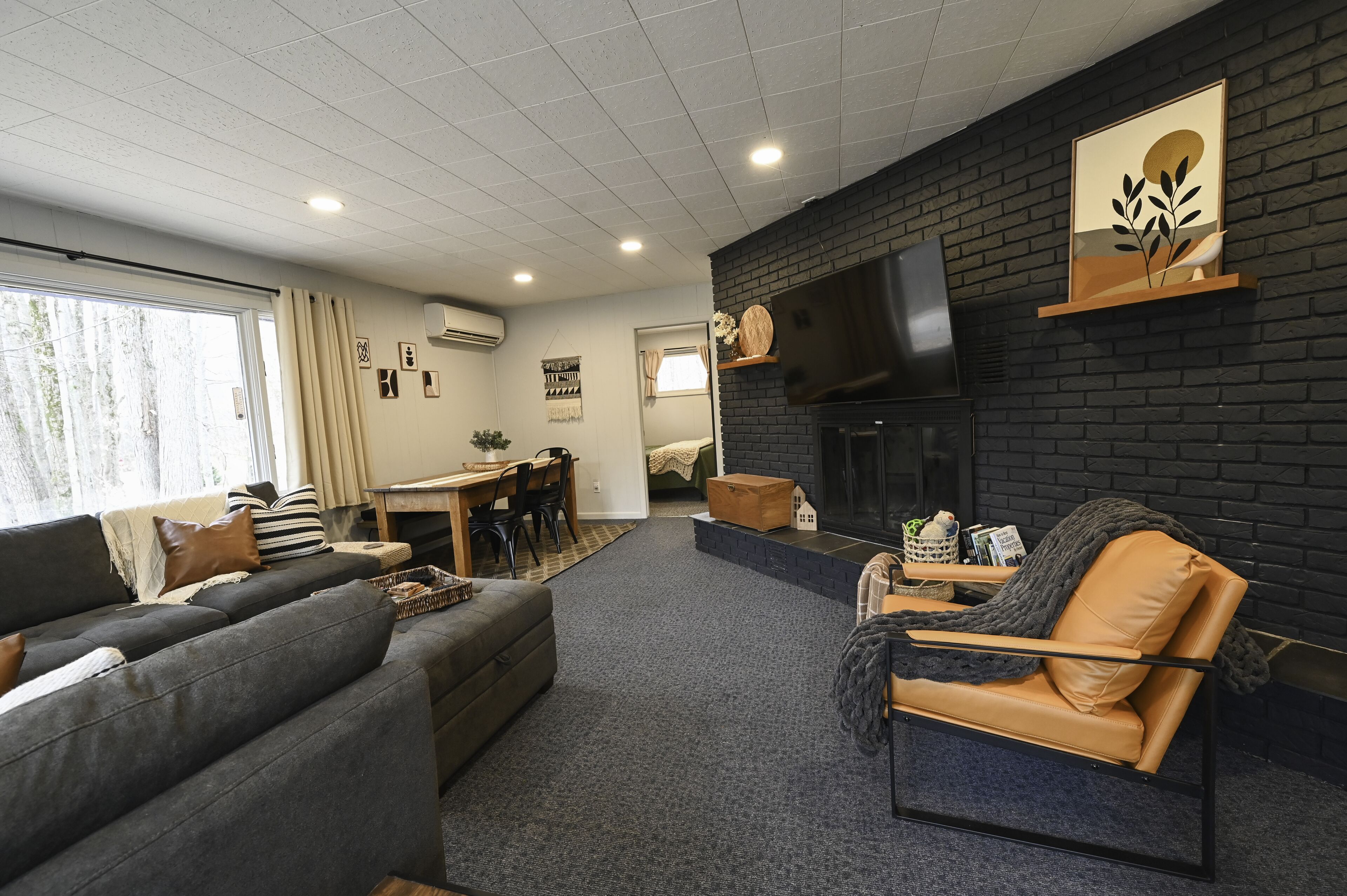 Un salon moderne avec un canapé, un fauteuil en cuir, une cheminée et un téléviseur fixé au mur.