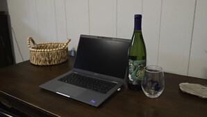 Una computadora portátil sobre una mesa de madera, con una cesta tejida y una botella de vino cerca.