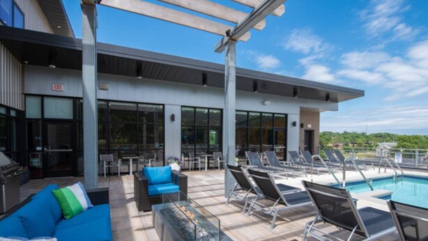A rooftop pool area with lounge chairs, a blue sofa, and a fire feature.