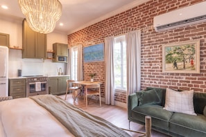 A modern kitchen with a built-in oven and microwave, a dining area with a table and chairs, a green sofa, and a chandelier. - Natchez Charm | 1/1 | Full Kitchen, King Bed, 2 Blocks from Mississippi River (Natchez)