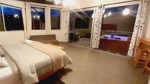 Een slaapkamer met een bed, een klein tafeltje en uitzicht op een zwembad door een schuifdeur.
