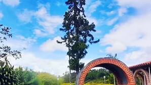 Een bakstenen bogenpoort met een bankje, omringd door een verzorgd gazon en bomen.