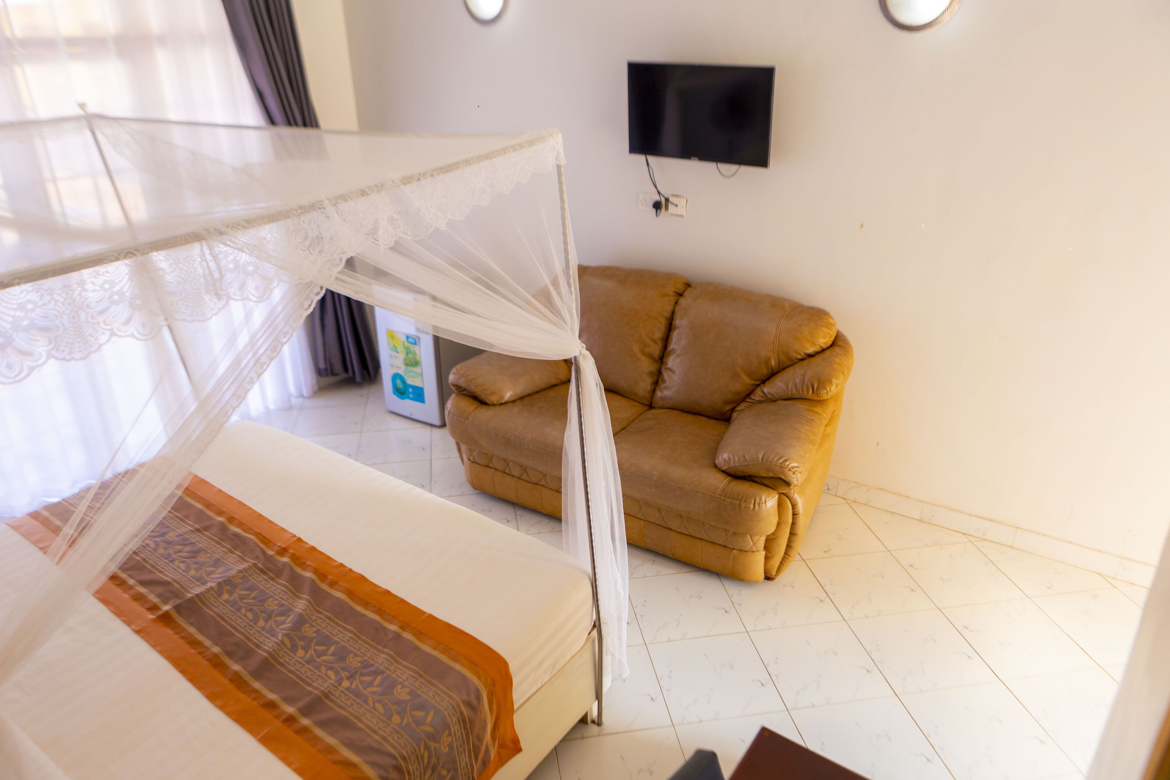 A bedroom with a bed, a sofa, a TV mounted on the wall, and a mosquito net over the bed.