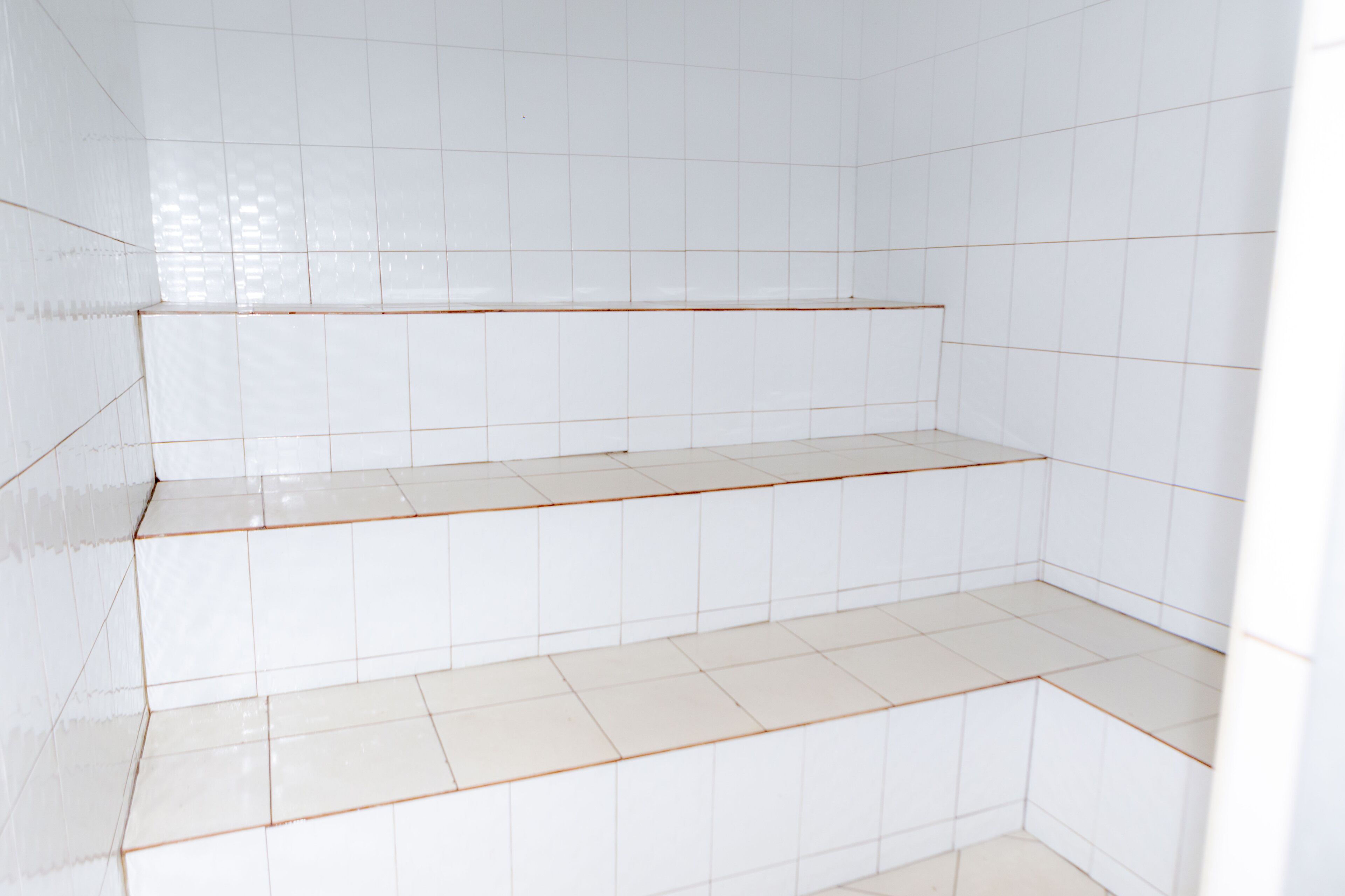 Um quarto com paredes e chão em azulejos brancos, com um lance de degraus dando acesso a um nível inferior.