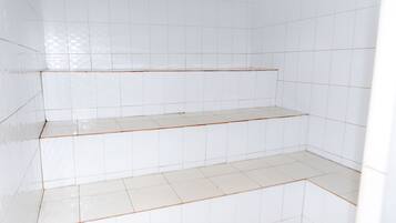 Um quarto com paredes e chão em azulejos brancos, com um lance de degraus dando acesso a um nível inferior.