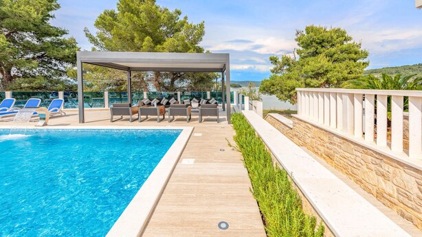 A poolside area with a covered seating area, lounge chairs, and a stone retaining wall.