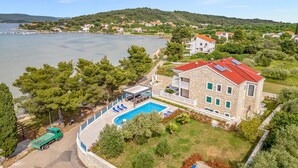 A stone building with a red roof, a swimming pool, and a view of a lake and hills.
