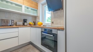 A modern kitchen with white cabinets, a built-in oven, a coffee maker, and a bowl of fruit.