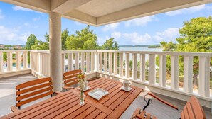 A covered outdoor seating area with wooden furniture and a view of the sea.