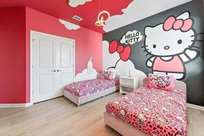 Quarto com duas camas, uma porta branca e um mural da Hello Kitty na parede.