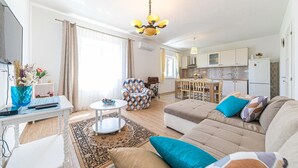 A well-lit living room with a sofa, a dining table, and a kitchen in the background. - 4 bedroom nice home in Kastel Novi (Kastel Novi)