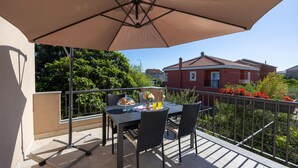 A balcony with a table and chairs, a large umbrella, and a view of a red building in the background. - 4 bedroom nice home in Kastel Novi (Kastel Novi)