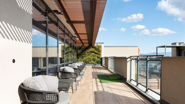 Terraza en la azotea con mobiliario exterior, pared verde y cielo despejado.