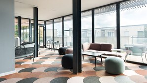 Un espace de détente moderne avec un sol à motifs géométriques, des sièges confortables et de grandes fenêtres offrant une vue sur le paysage urbain.