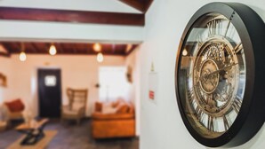 Une pièce dotée d’une grande horloge décorative au mur, d’un plafond en bois et d’un coin salon confortable avec un canapé et des fauteuils.