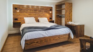 Une chambre moderne avec une tête de lit en bois, un lit recouvert de linge de maison blanc, une table de chevet et un porte-manteau mural.