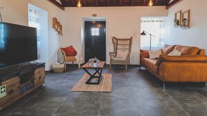 Un salon confortable avec un téléviseur, un fauteuil en osier, un canapé en cuir et un meuble en bois.