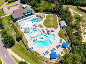 An aerial view of a resort with a large pool, sun loungers, a water slide, and a building with a green roof. - CC302E Emerald Shores * Pool/Lazy River/Splash Pad (Kill Devil Hills)