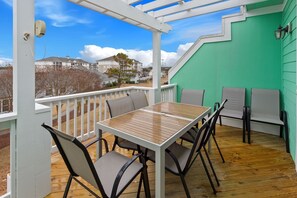 A covered outdoor area with a table and chairs, a green wall, and a view of houses in the background. - CC302E Emerald Shores * Pool/Lazy River/Splash Pad (Kill Devil Hills)