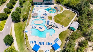 Luchtbeeld van een resort met een groot zwembad, ligbedden, een glijbaan en een gebouw met een groen dak.
