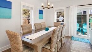 A dining area with a wooden table, wicker chairs, and a chandelier. - Luxury OBX 3BR, Private Hot Tub, Near the Beach (Corolla)
