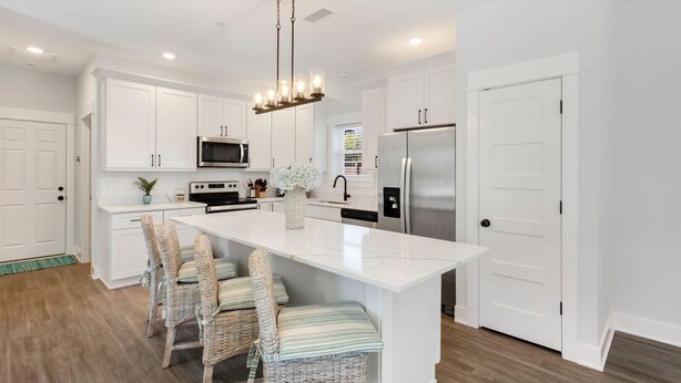 A modern kitchen with white cabinetry, stainless steel appliances, a central island with bar stools, and a pendant light fixture. - Luxury OBX 3BR, Private Hot Tub, Near the Beach (Corolla)