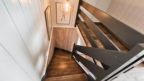 Eine Holztreppe mit schwarzer Handlauf, weißen Wänden und einer hängenden Leuchte.