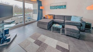 Una sala moderna con un sofá seccional, un televisor de pantalla plana, una mesa de centro y un ventanal con vistas a un estacionamiento.