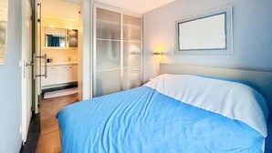Un dormitorio con cama, una puerta corredera que da a un baño y una lámpara fijada en la pared.