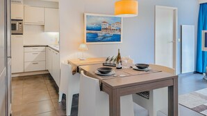 Cocina compacta con comedor, un cuadro de una escena costera y una mesa para dos con vino y copas.