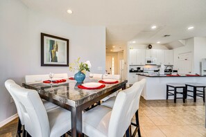 A dining area with a marble table, white chairs, and a vase with flowers. - 5BR Family Villa w/ Saltwater Pool near Disney (Davenport)