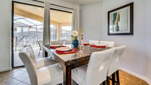Comedor con una mesa de mármol, sillas blancas y puerta de vidrio que da a un patio exterior.