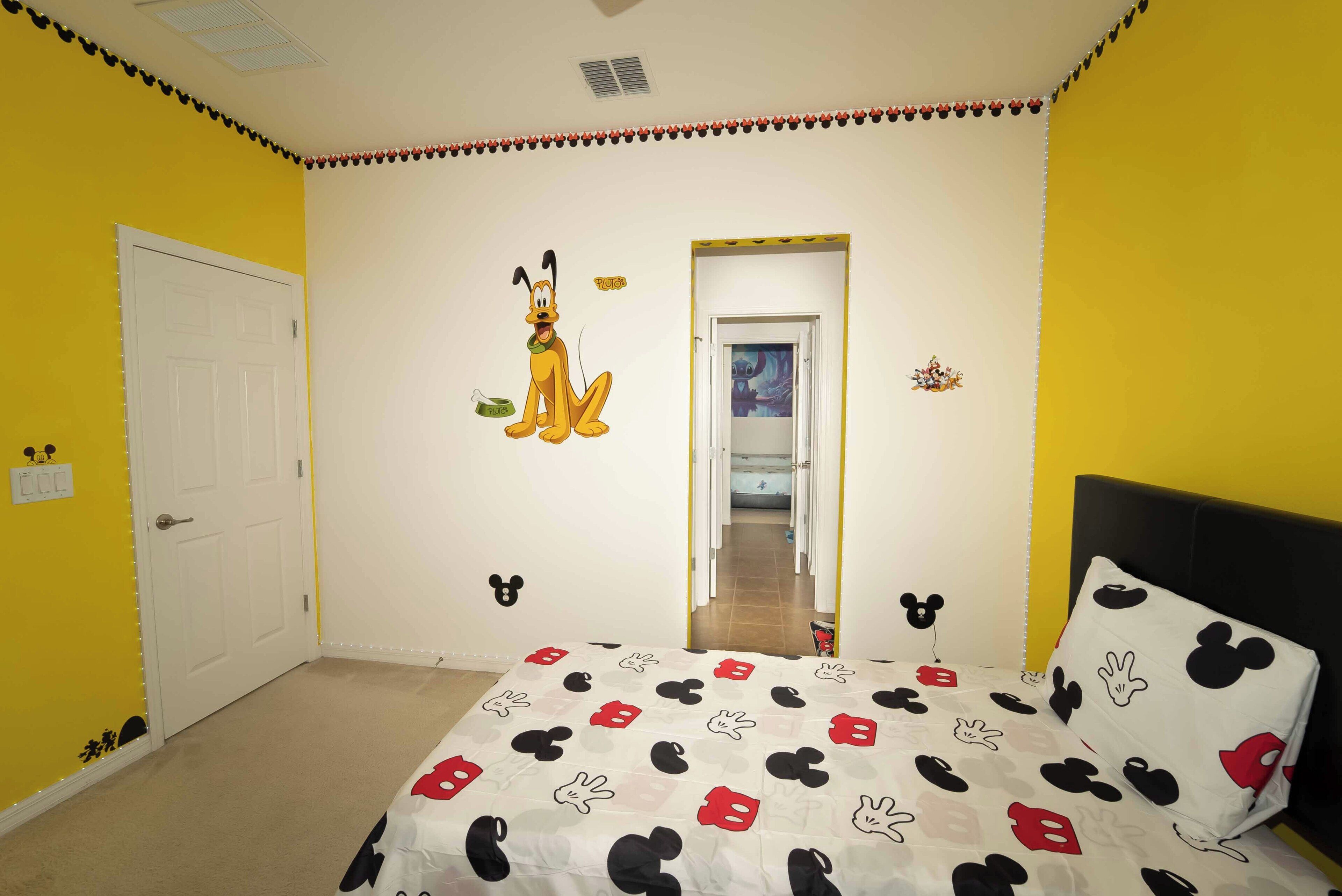 A room with a bed, a door, and a wall with Mickey Mouse decorations.