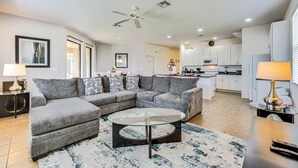 A modern living room with a sectional sofa, a glass coffee table, and a kitchen in the background.