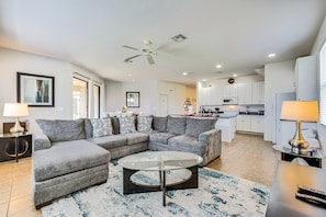 A modern living room with a sectional sofa, a glass coffee table, and a kitchen in the background. - 5BR Family Villa w/ Saltwater Pool near Disney (Davenport)