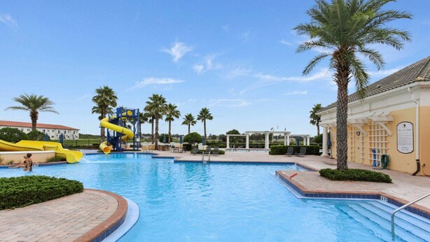 A swimming pool with a water slide, palm trees, and a covered area with lounge chairs.