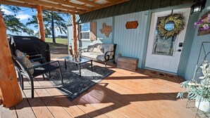 A covered porch with a grill, outdoor seating, and a door with a wreath. - Rosie's Ranch Retreat - Farm Stay (Ben Wheeler)