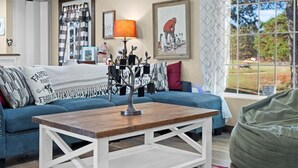 A living room with a blue sofa, a wooden coffee table, and a window with a view of the outdoors. - Rosie's Ranch Retreat - Farm Stay (Ben Wheeler)