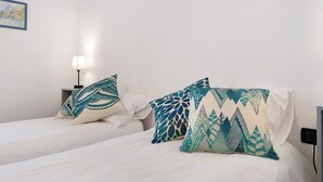 Hotellihuoneessa on kaksi sänkyä, joissa on valkoiset päiväpeitteet ja koristeelliset tyynyt. Huoneessa on yöpöytä, jossa on lamppu, sekä seinään kiinnitetty pistorasia.