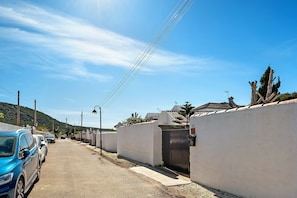 Une rue résidentielle bordée de voitures garées, avec un mur blanc et un portail.