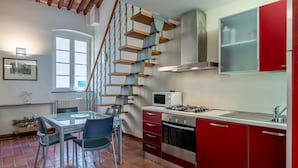 A kitchen with a red and white color scheme, a gas stove, a microwave, and a staircase with wooden steps. - Toro's Home Lucca Apartment with Wi-Fi and Air Conditioning (Lucca)